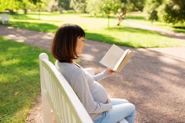 Счастливая беременная азиатка читает книгу в парке — стоковое фото