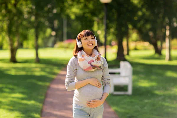 Gelukkig zwangere Aziatische vrouw hoofdtelefoon in park — Stockfoto