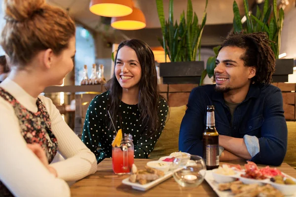Happy friends with drinks and food at bar or cafe — Stock Photo, Image