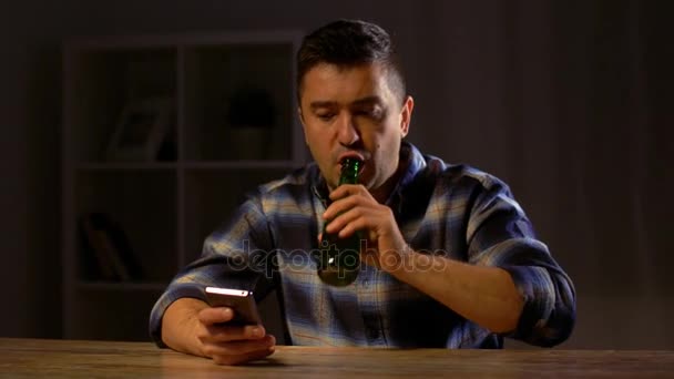 Hombre con teléfono inteligente beber cerveza embotellada en casa — Vídeo de stock