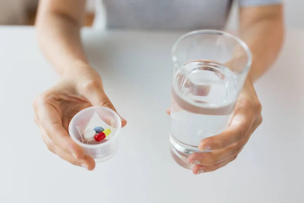 Perto de mãos com pílulas e vidro de água — Fotografia de Stock