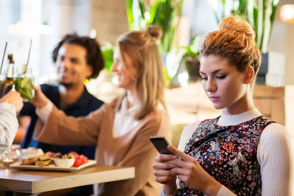 Nő a smartphone és a barátok étteremben — Stock Fotó