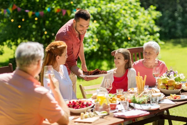 Счастливая семья с ужином или вечеринкой в летнем саду — стоковое фото