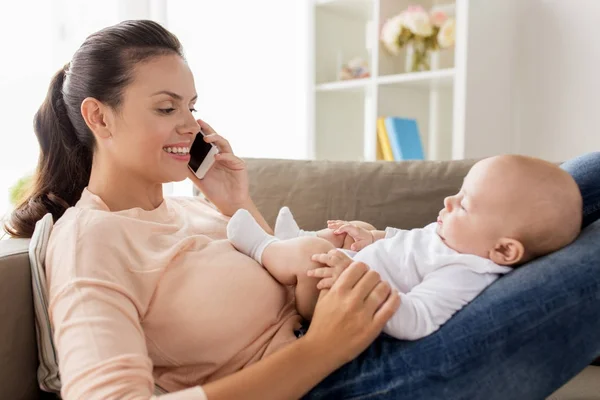 Moeder met baby opgeroepen smartphone thuis Stockafbeelding