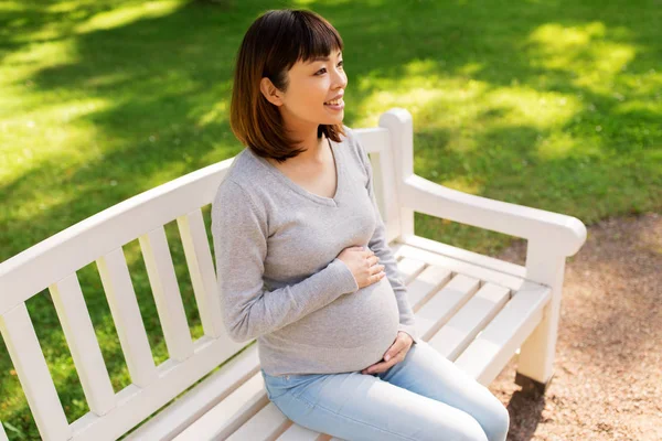 Happy pregnant asian woman sitting on park bench — Stock Photo, Image