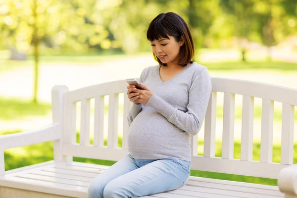 Glücklich schwangere Asiatin mit Smartphone im Park — Stockfoto