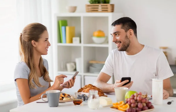 Casal com smartphones tomando café da manhã em casa — Fotografia de Stock