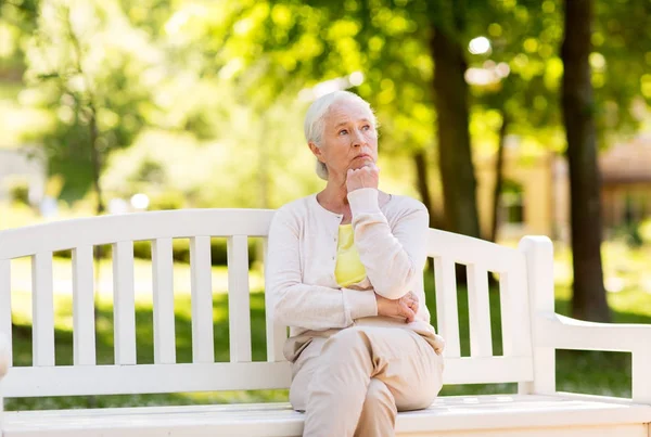 Грустная пожилая женщина сидит на скамейке в летнем парке — стоковое фото
