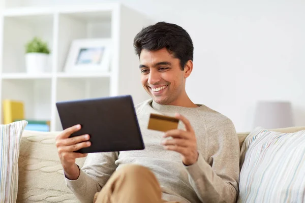 Hombre sonriente con tablet PC y tarjeta de crédito en casa —  Fotos de Stock