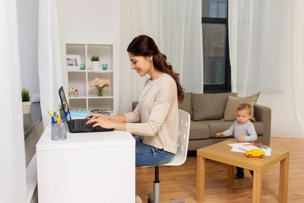 Glückliche Mutter mit Baby und Laptop, die zu Hause arbeitet lizenzfreie Stockfotos