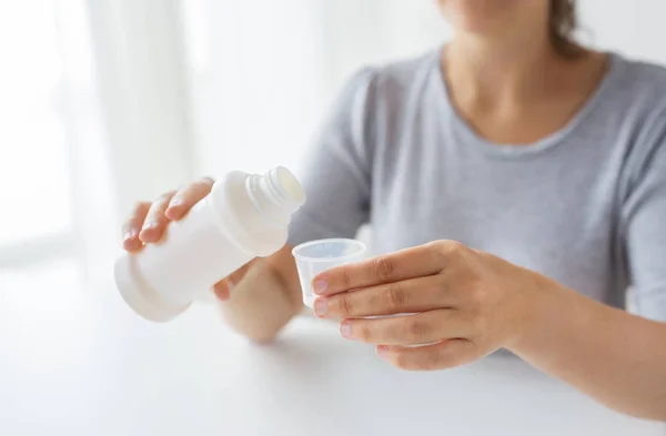Mulher derramando xarope de garrafa para copo de remédio — Fotografia de Stock