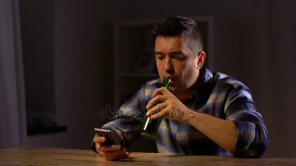 Homem com smartphone bebendo cerveja engarrafada em casa — Vídeo de Stock