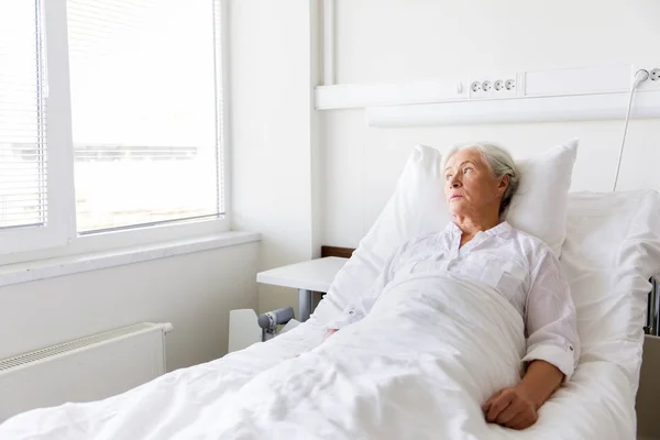 Грустная старшая женщина лежит на кровати в больнице — стоковое фото