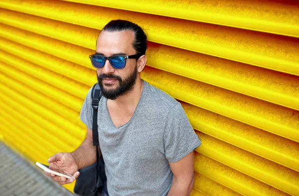 Ο άνθρωπος σε γυαλιά ηλίου με smartphone και τσάντα στον τοίχο — Φωτογραφία Αρχείου
