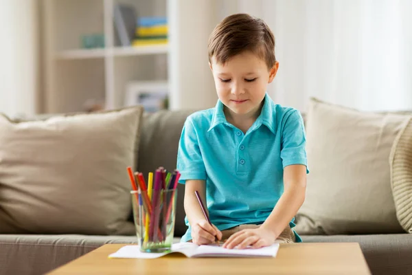 Pojke med anteckningsbok och pennor ritning hemma — Stockfoto