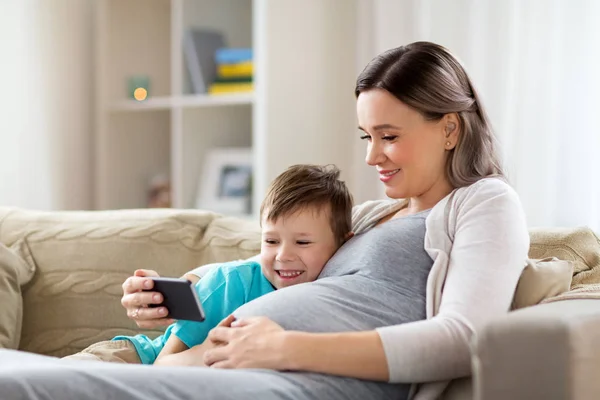 Zwangere moeder en zoon met smartphone thuis — Stockfoto