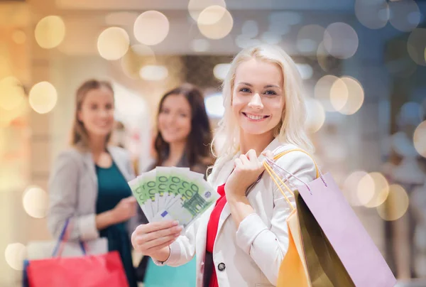 Mulheres jovens com sacos de compras e dinheiro no shopping — Fotografia de Stock