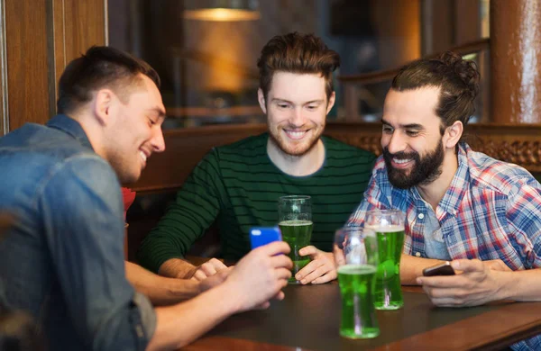 Amigos com smartphone bebendo cerveja verde no pub — Fotografia de Stock