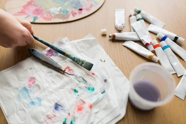 Mão artista com pincel, papel e tubos de pintura — Fotografia de Stock