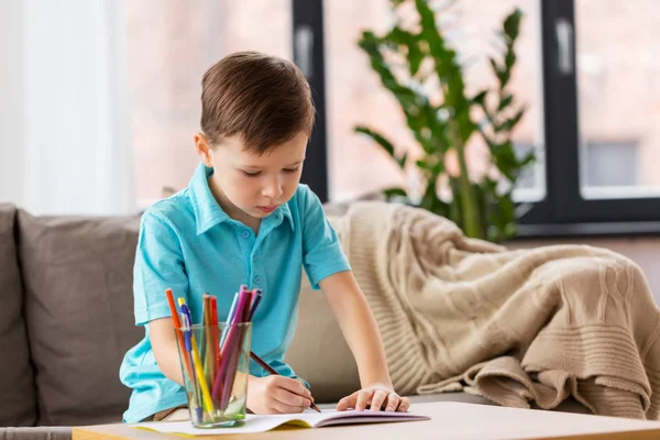 Jongen met notitieboekje en potloden tekening thuis — Stockfoto