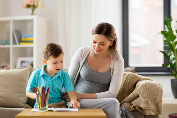 Madre embarazada e hijo con cuaderno de trabajo en casa —  Fotos de Stock