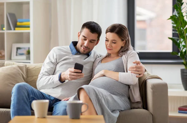 Mann und schwangere Frau mit Smartphone zu Hause — Stockfoto