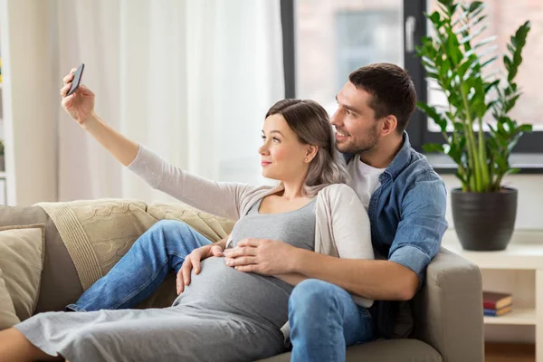 Mężczyzna i kobieta w ciąży, biorąc selfie w domu — Zdjęcie stockowe