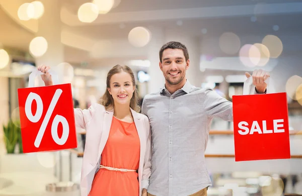 Feliz jovem casal com sacos de compras vermelhas no shopping — Fotografia de Stock