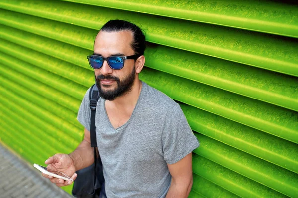 Hombre en gafas de sol con smartphone y bolsa en la pared —  Fotos de Stock
