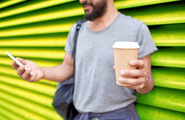 コーヒー カップと壁にスマート フォンを持つ男 — ストック写真