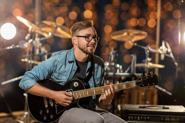 Музыкант играет на гитаре в студии при свете — стоковое фото