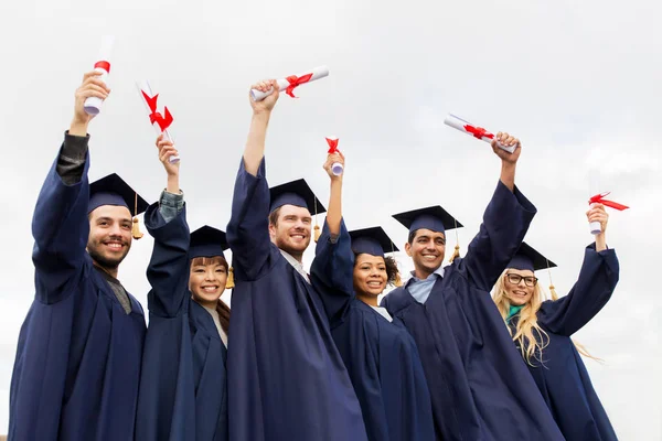 Happy students in mortar boards with diplomas — Stock Photo, Image