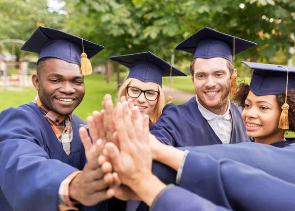 Happy students in mortar boards making high five — Stock Photo, Image