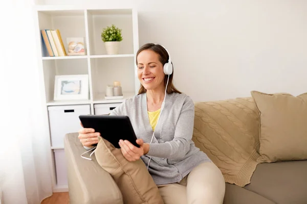 Mulher feliz com tablet pc e fones de ouvido em casa — Fotografia de Stock