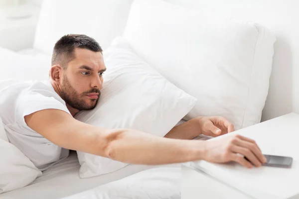 Mladý muž sáhl pro smartphone v posteli — Stock fotografie