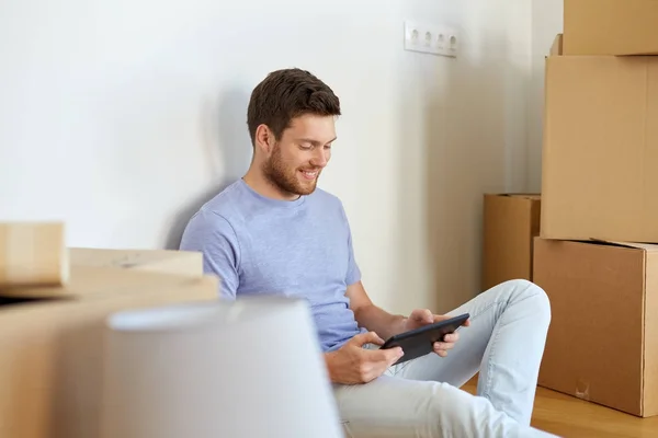Человек с планшетным компьютером и коробками переезжает в новый дом — стоковое фото
