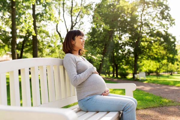 Happy pregnant asian woman sitting on park bench — Stock Photo, Image