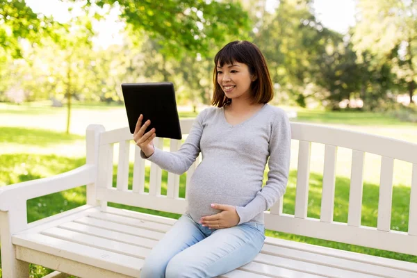 Szczęśliwy w ciąży asian kobieta z komputera typu tablet w parku — Zdjęcie stockowe