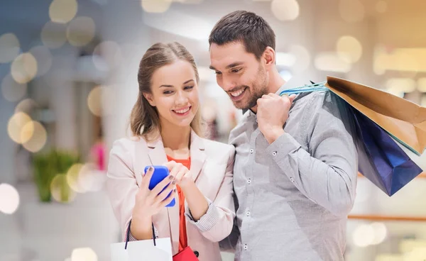 Casal com smartphone e sacos de compras no shopping — Fotografia de Stock