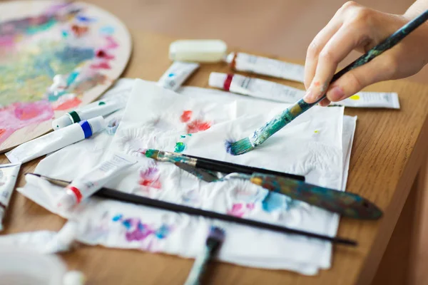 Hand van de kunstenaar met penseel, papier en verf buizen — Stockfoto