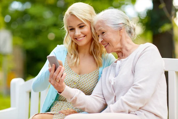 Dotter och senior mor med smartphone på park — Stockfoto