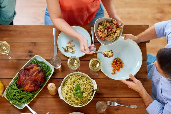 Människor som äter sallad vid bord med mat — Stockfoto