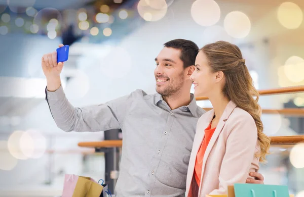 Happy couple with smartphone taking selfie in mall — Stock Photo, Image
