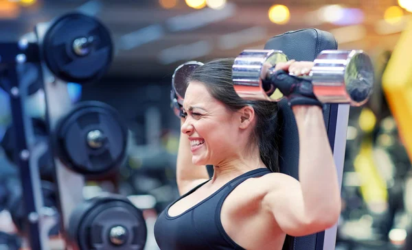 Mujer joven flexionando músculos con mancuerna en el gimnasio —  Fotos de Stock