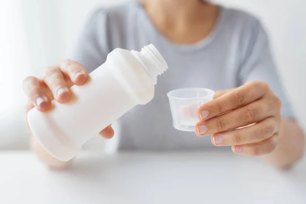 Женщина наливает сироп из бутылки в чашку с лекарствами — стоковое фото