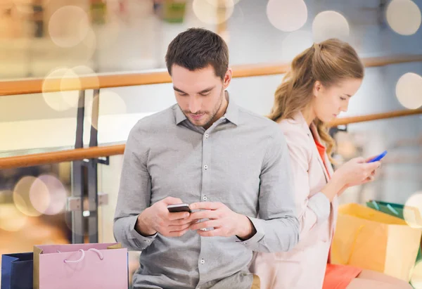 Couple with smartphones and shopping bags in mall — Stock Photo, Image