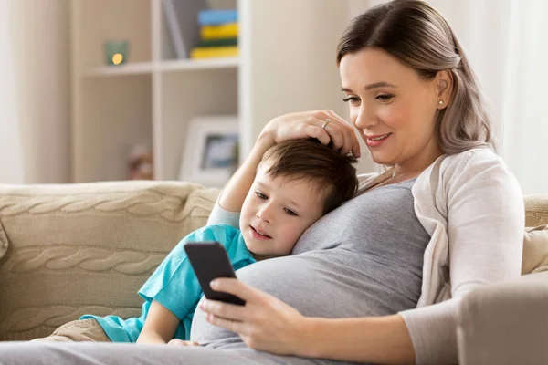 Zwangere moeder en zoon met smartphone thuis — Stockfoto