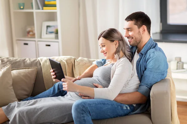 Man en zwangere vrouw met tablet pc thuis — Stockfoto