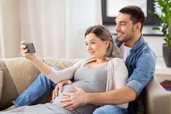 Homem e mulher grávida tomando selfie em casa — Fotografia de Stock