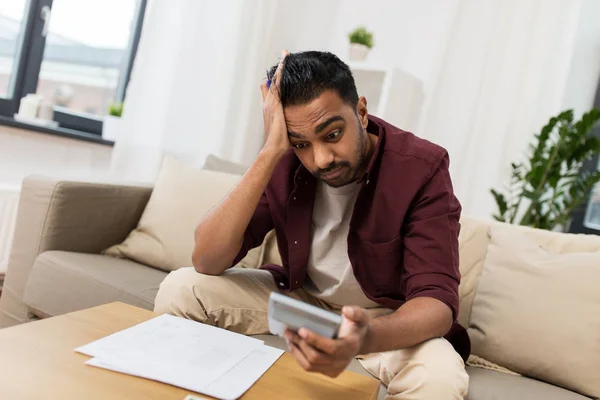 Confused man with papers and calculator at home — Stock Photo, Image